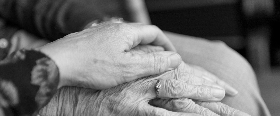 Een jongere hand houdt zorgzaam de handen van een oudere vast